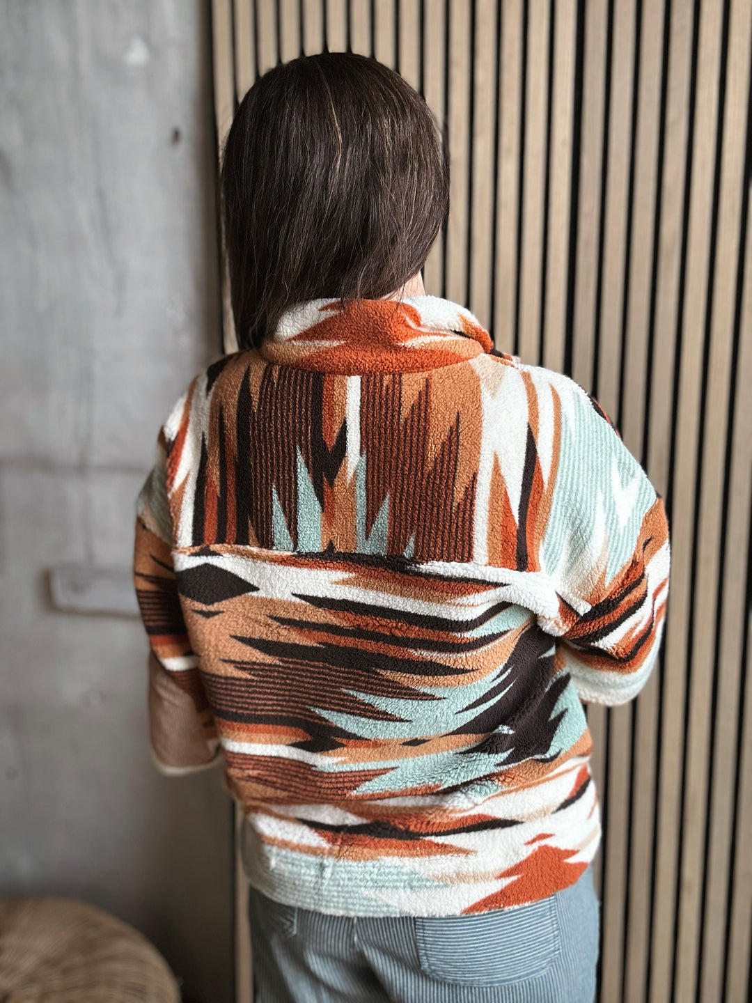 Person wearing a patterned sweater standing against a neutral wall.