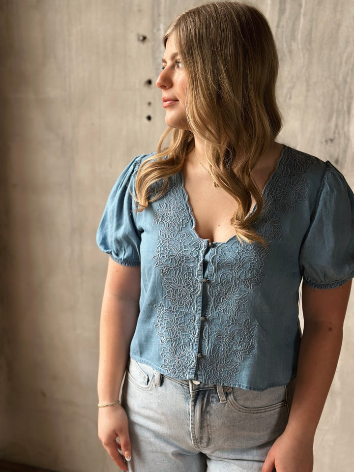 Woman wearing a blue embroidered top and jeans against a neutral background