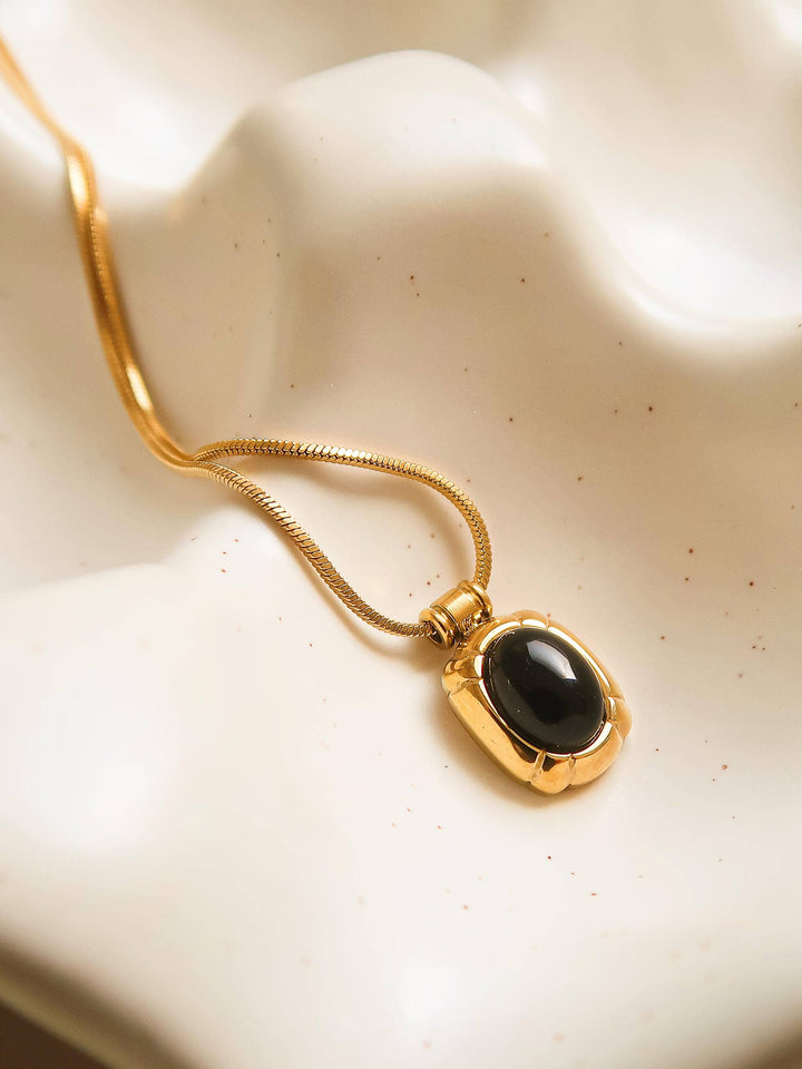 Gold necklace with a black pendant on a beige background