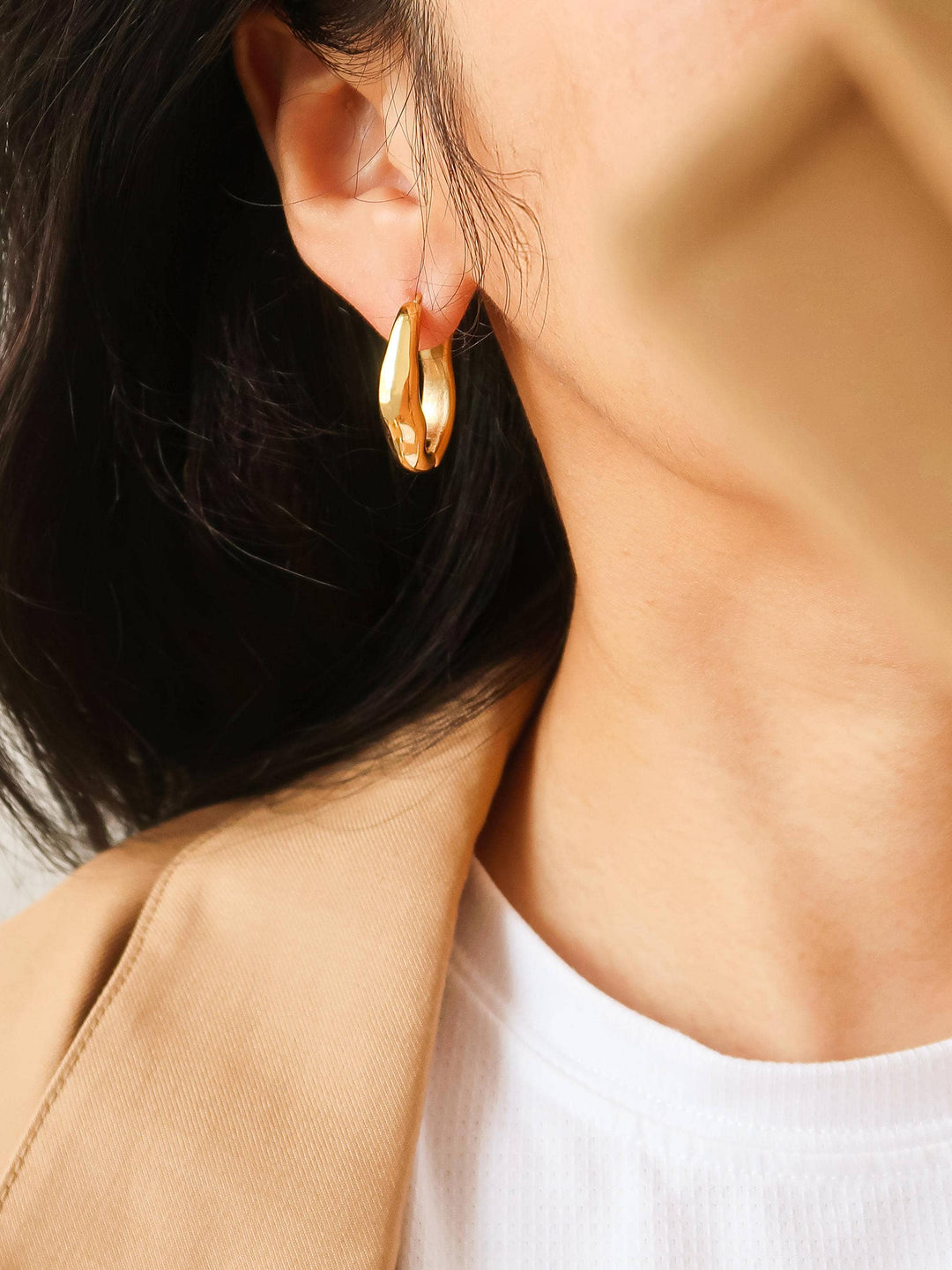 Close-up of a person wearing gold hoop earrings with a neutral background