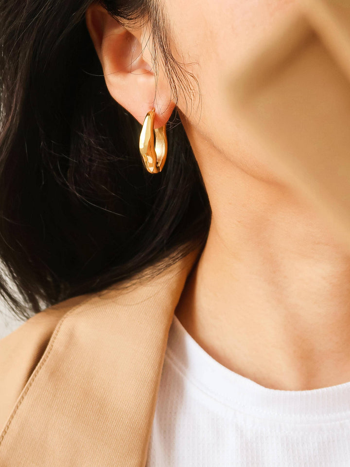 Close-up of a person wearing gold hoop earrings with a neutral background