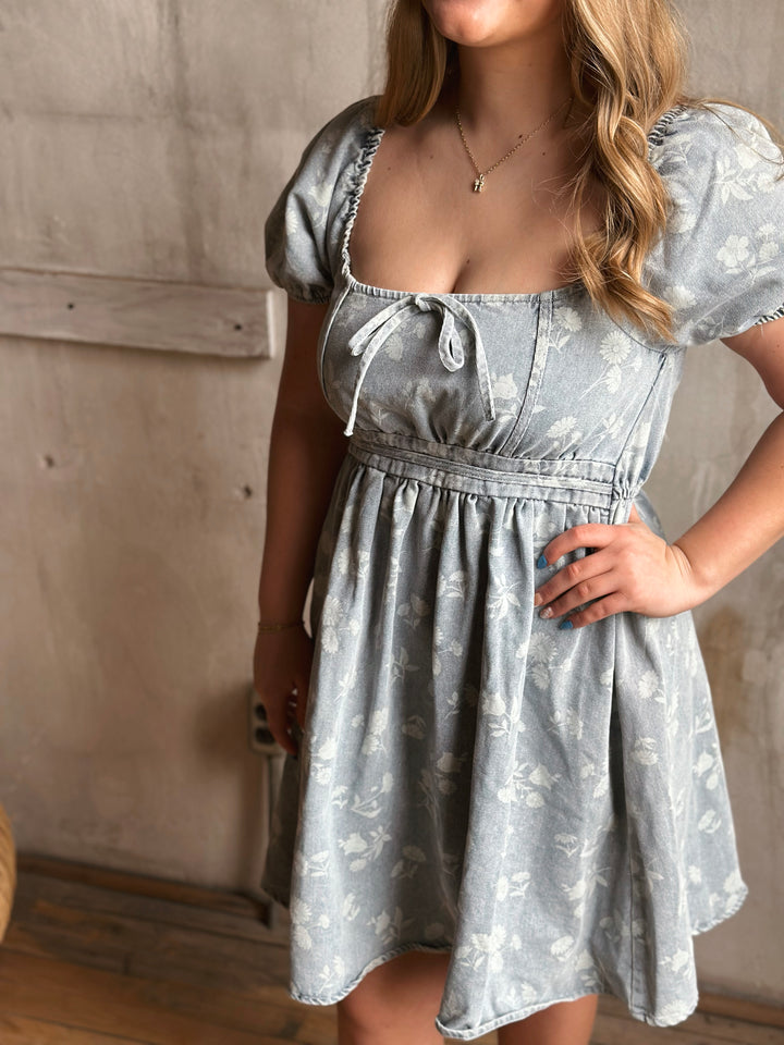 Woman wearing a light blue denim floral dress against a neutral background