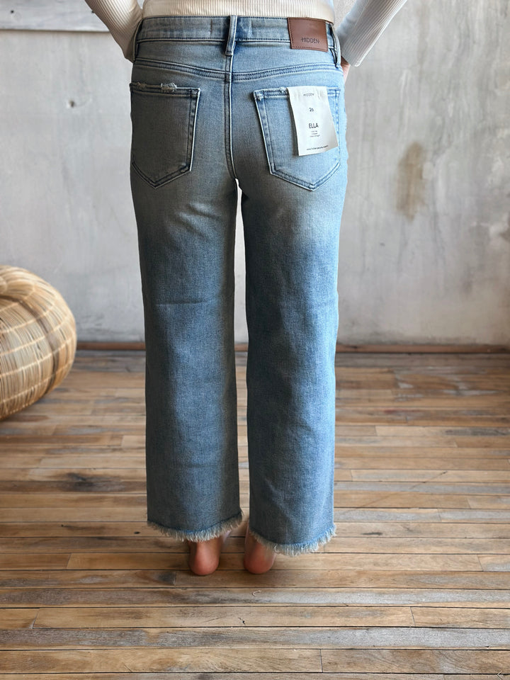 Person wearing light blue jeans with a wooden floor and woven basket in the background