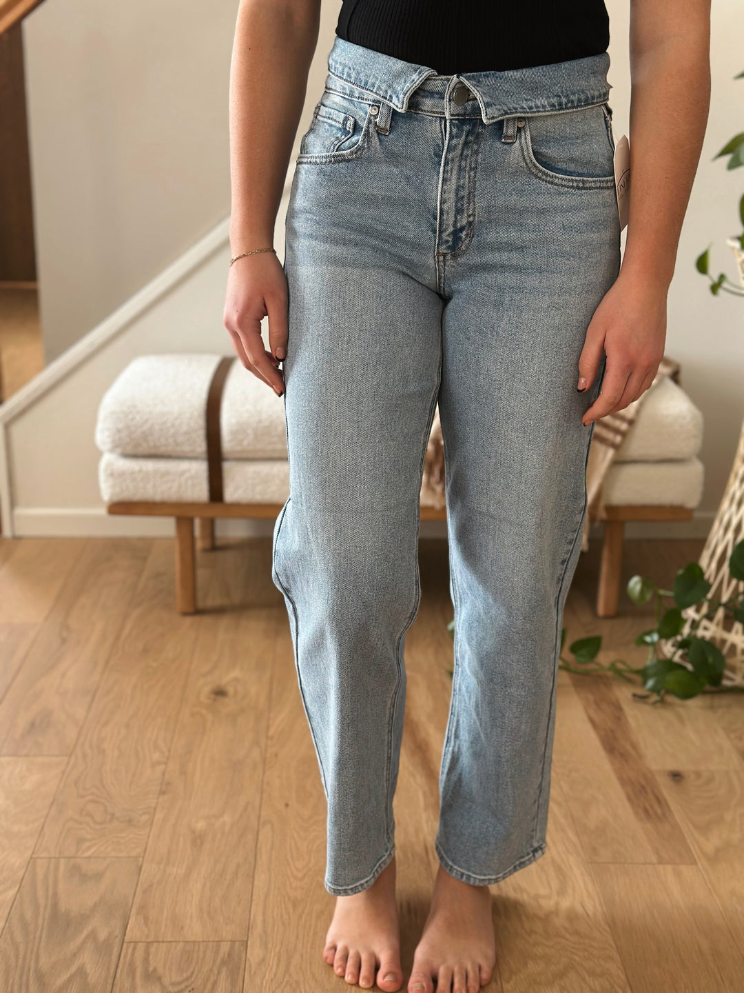 Person wearing light blue jeans standing in a room with wooden flooring and a staircase.