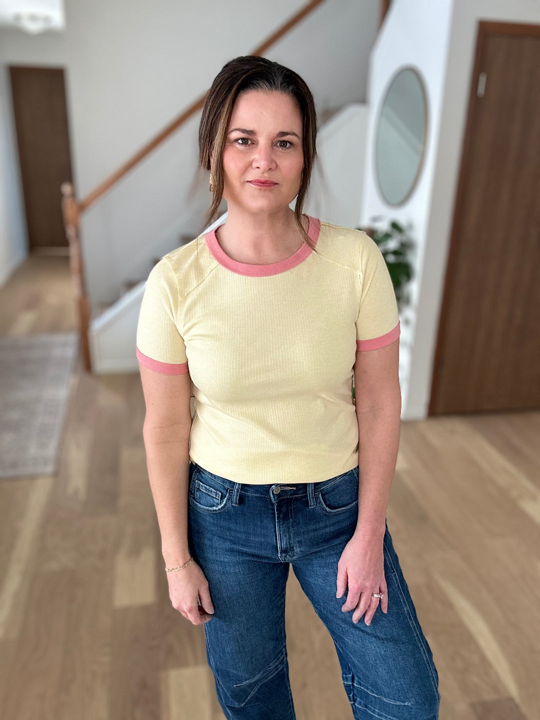 Woman wearing a yellow shirt with pink trim and blue jeans indoors.