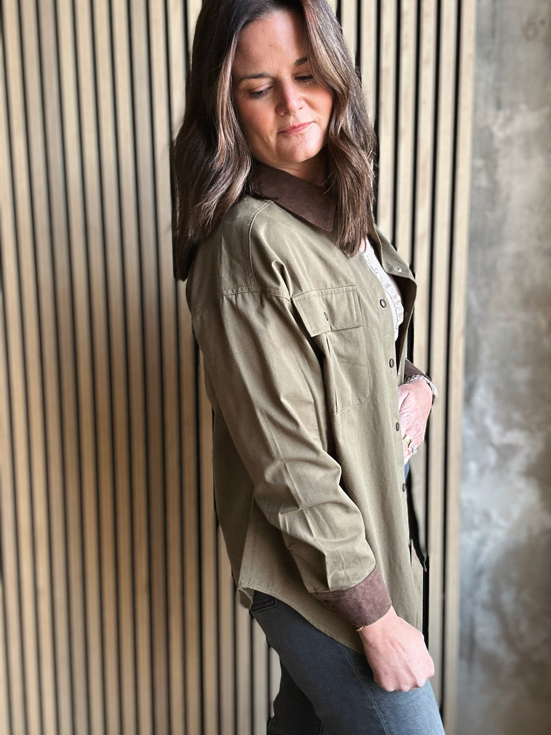 Woman wearing a green shirt and dark pants leaning against a striped wall.