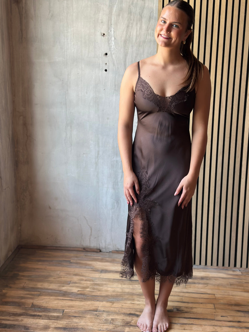 Woman wearing a chocolate brown satin slip midi dress with lace trim and a side slit, front view