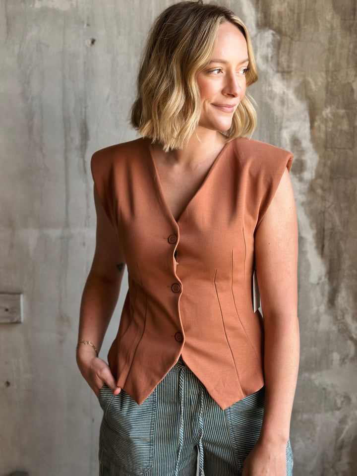 Woman wearing a brown sleeveless blazer against a concrete wall.