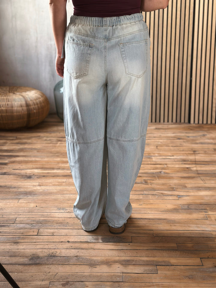 Person wearing light blue wide-leg pants on a wooden floor.