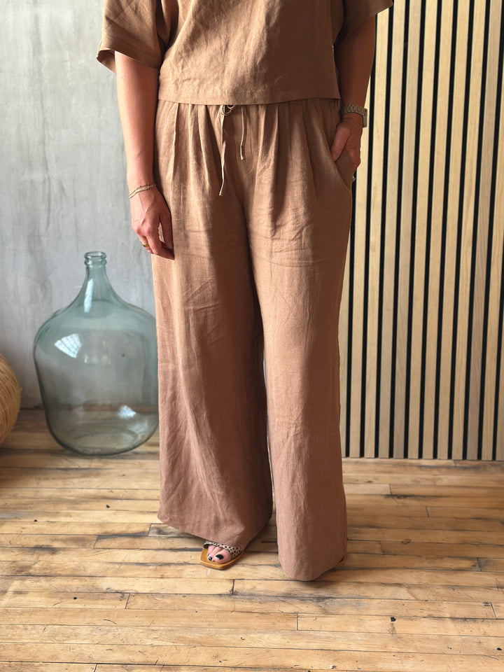 A person wearing brown pants standing in a room with a wooden floor and striped wall.