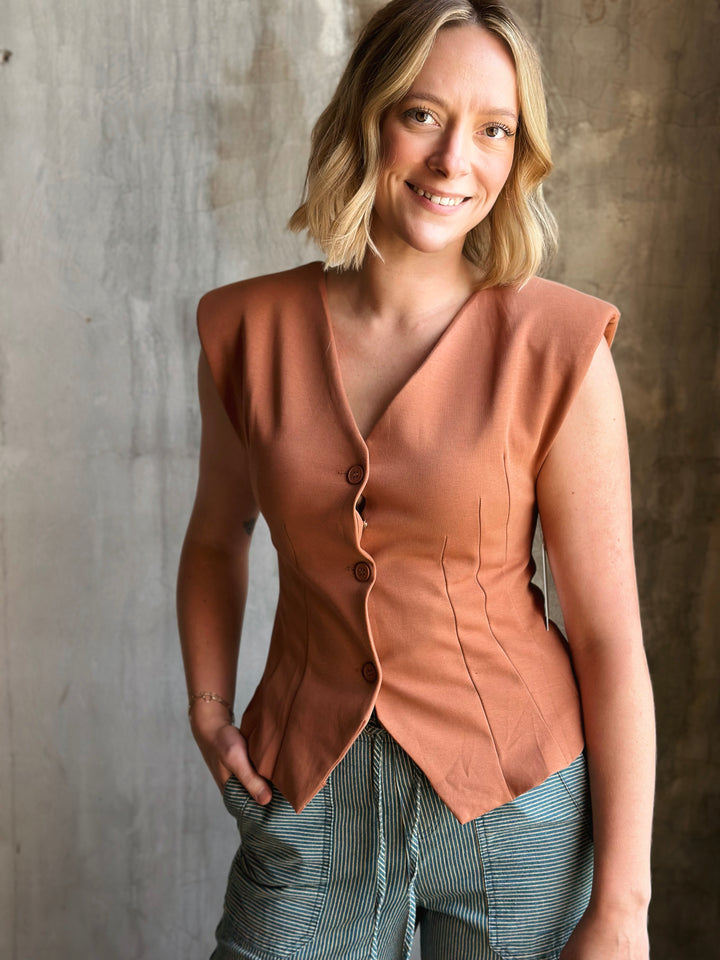 Woman wearing a brown sleeveless blazer against a textured wall.