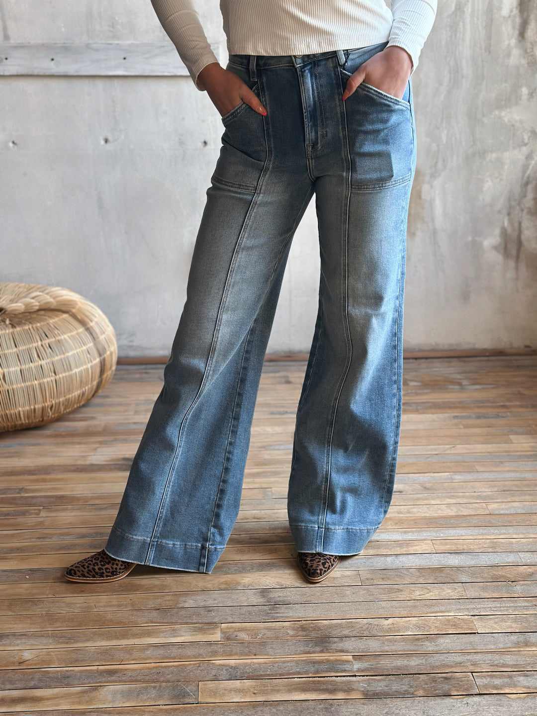Person wearing blue flared jeans standing on a wooden floor with a woven basket in the background.