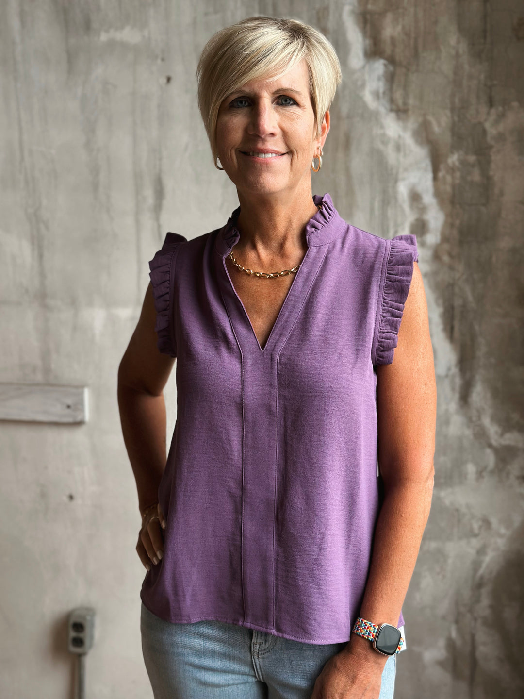 Woman wearing a purple sleeveless top standing against a textured wall.