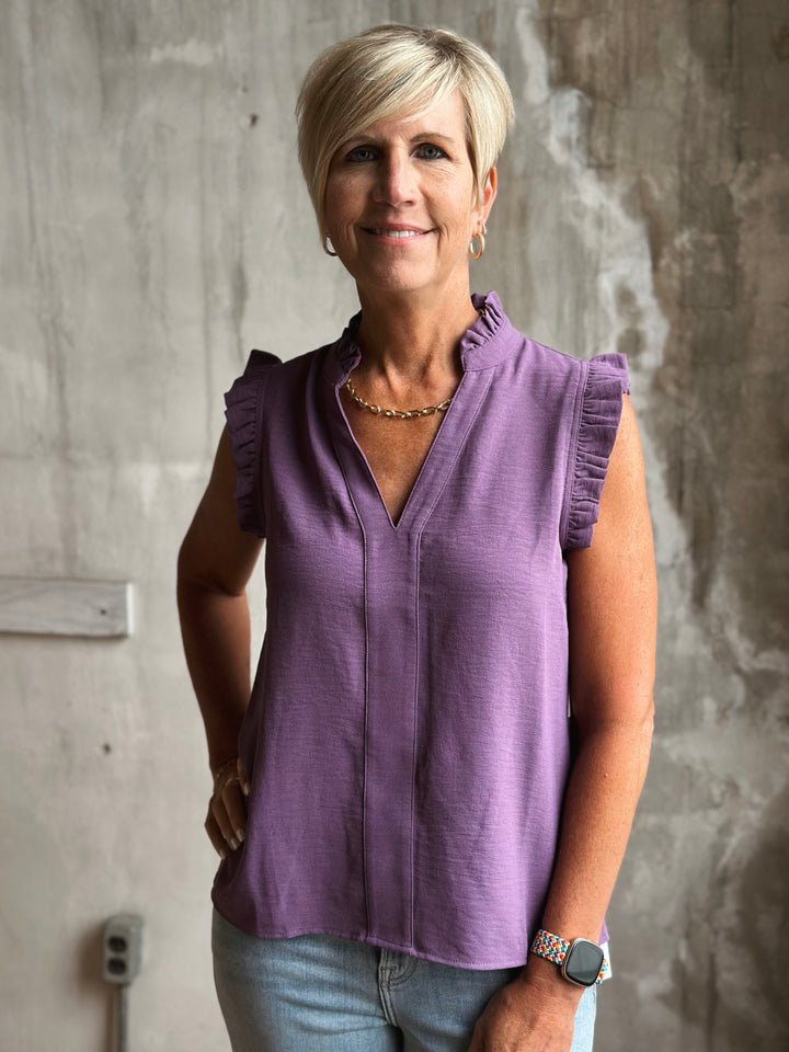 Woman wearing a purple sleeveless top standing against a textured wall.