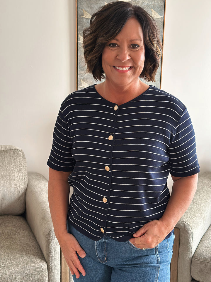 Woman wearing a navy striped shirt with buttons, standing in a room with a couch and wall art.