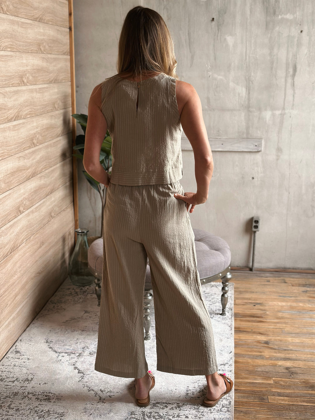 Woman wearing a sage sleeveless top and matching wide-leg pants in a room with wooden floor and concrete wall.