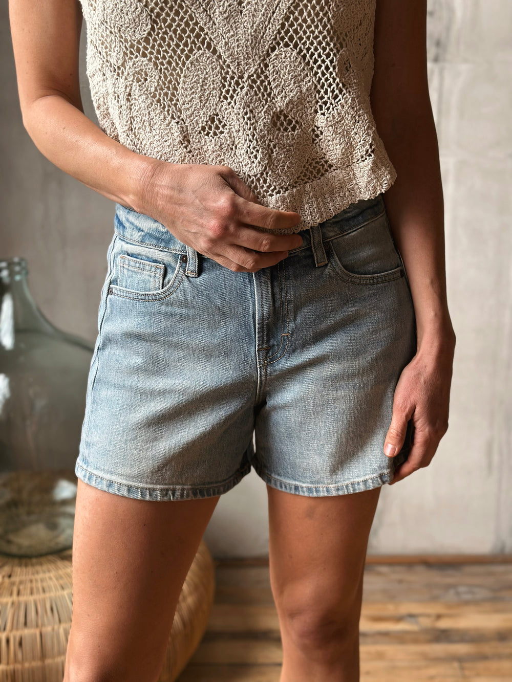Person wearing a textured top and light washed denim shorts in a casual setting.