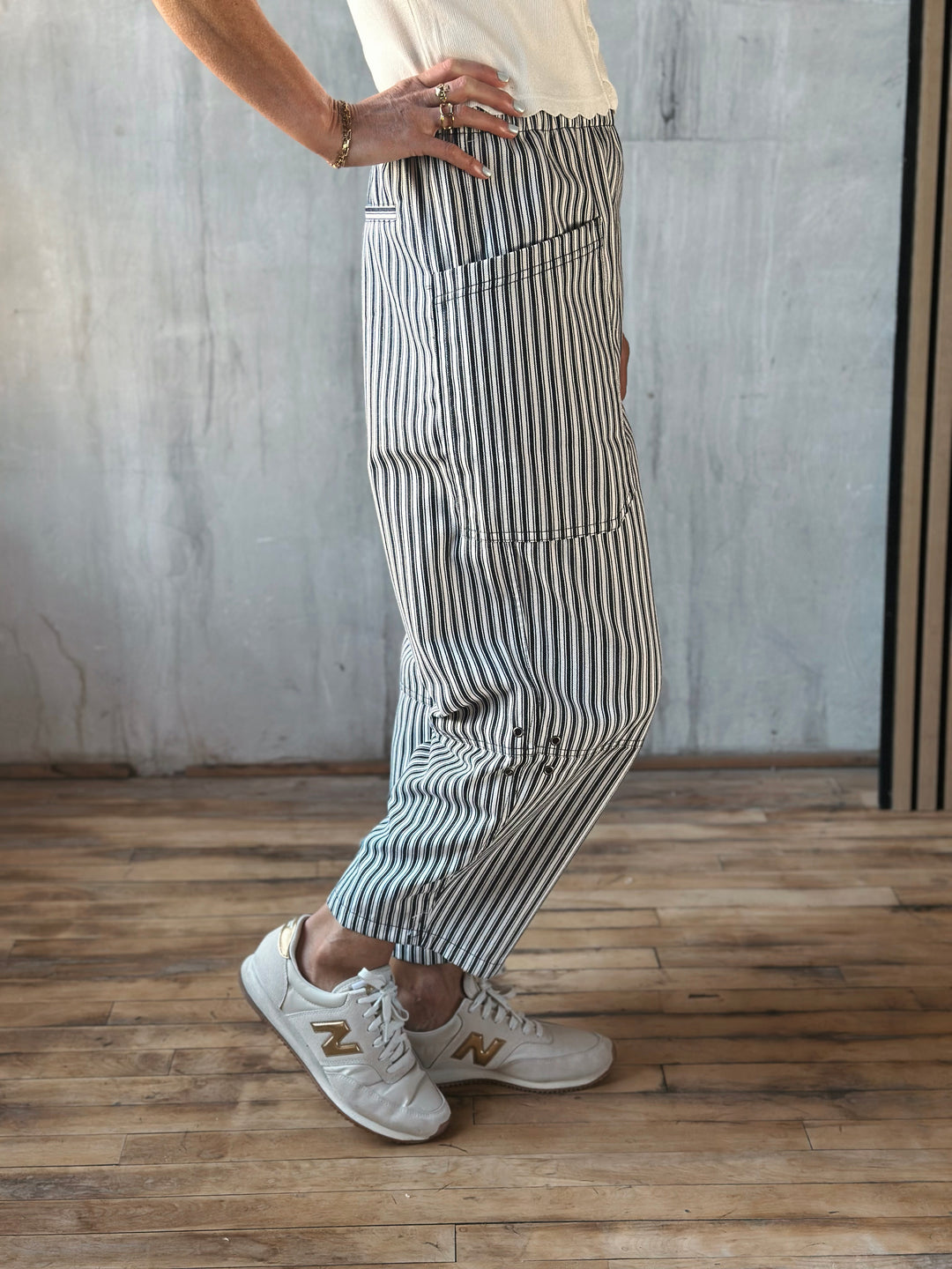 Person wearing striped pants and white sneakers in a room with wooden floor and gray wall.