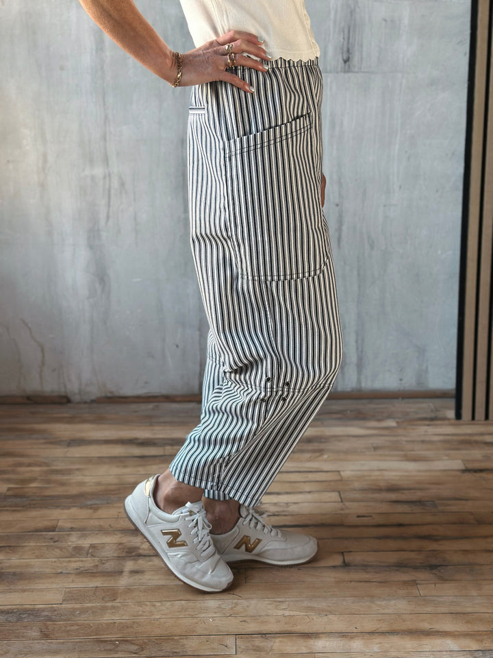 Person wearing striped pants and white sneakers in a room with wooden floor and gray wall.