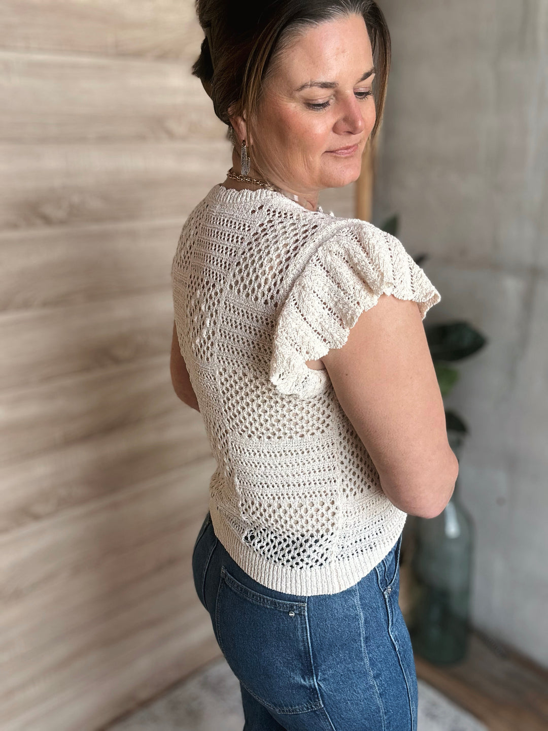 Woman wearing a white crochet top and blue jeans indoors.