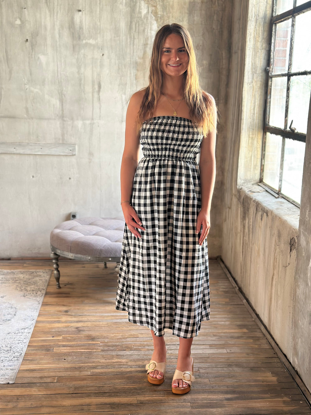 Woman wearing a black and white plaid strapless dress in a room with wooden floor and large window.