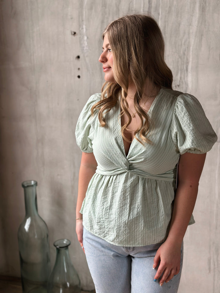 Woman wearing a light green blouse with puffed sleeves against a neutral background
