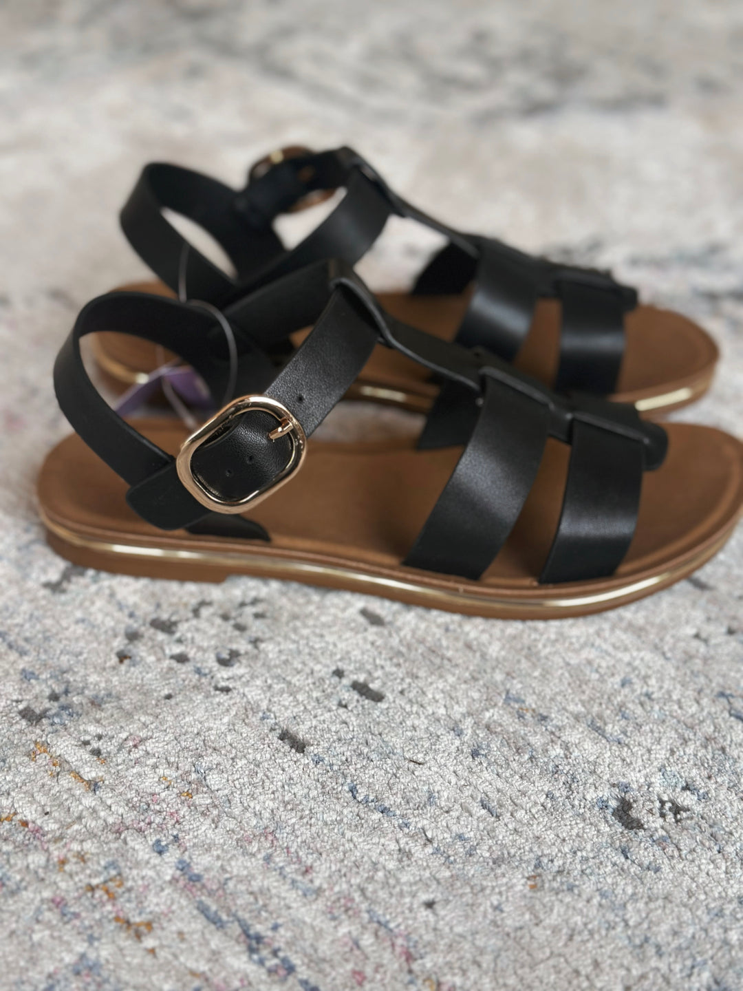 Black strappy sandals on a textured gray surface