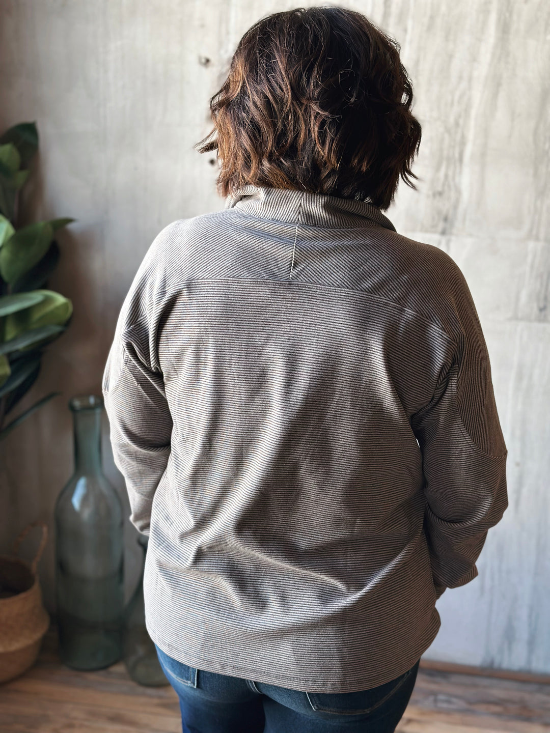 Person wearing a gray jacket standing in a room with a wooden floor and light-colored walls.