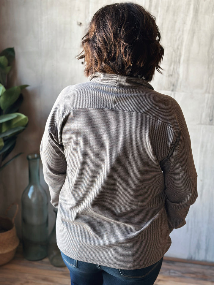 Person wearing a gray jacket standing in a room with a wooden floor and light-colored walls.