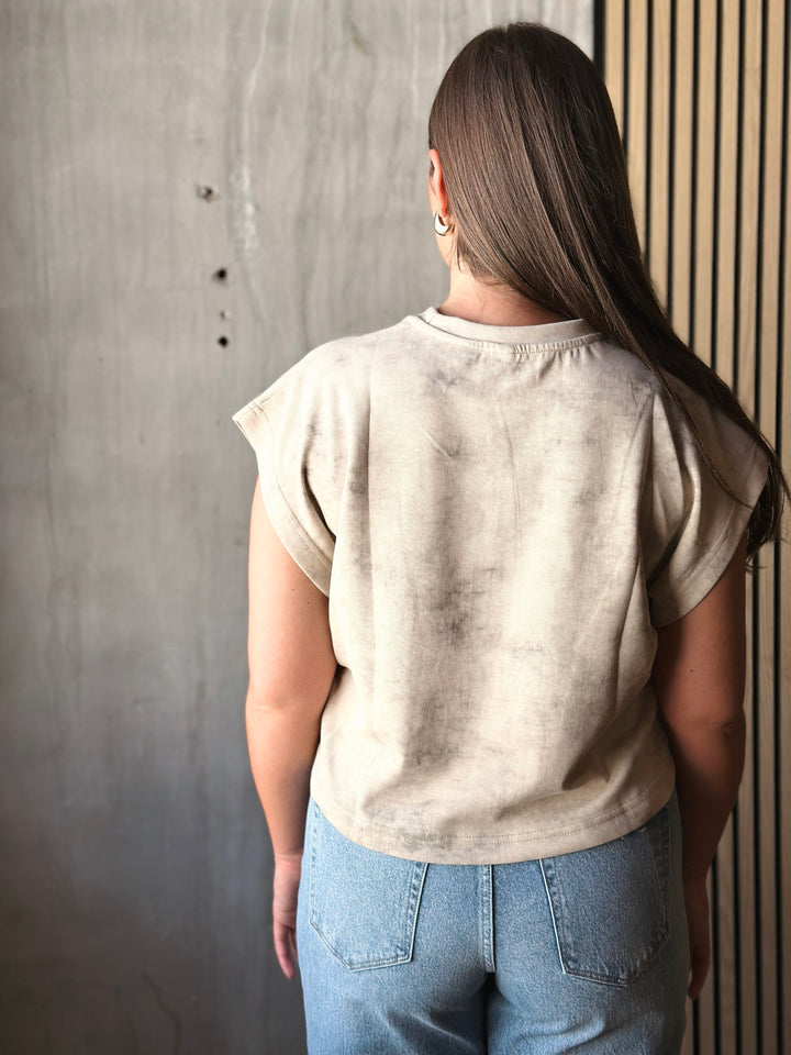 Person wearing a beige top and blue jeans against a gray wall.