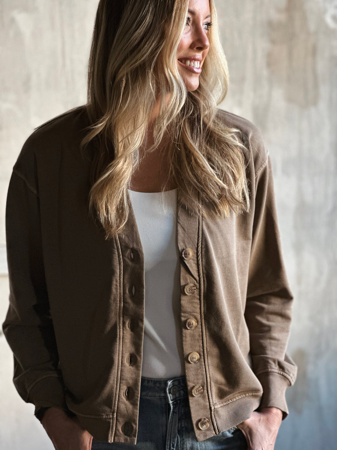 Woman wearing a brown jacket over a white top with a neutral background