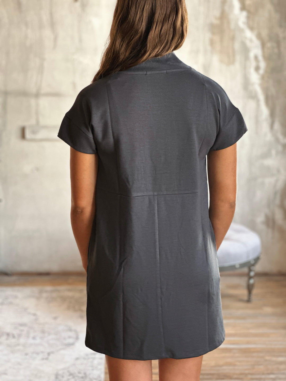 A person wearing a dark gray dress with short sleeves in a neutral setting.