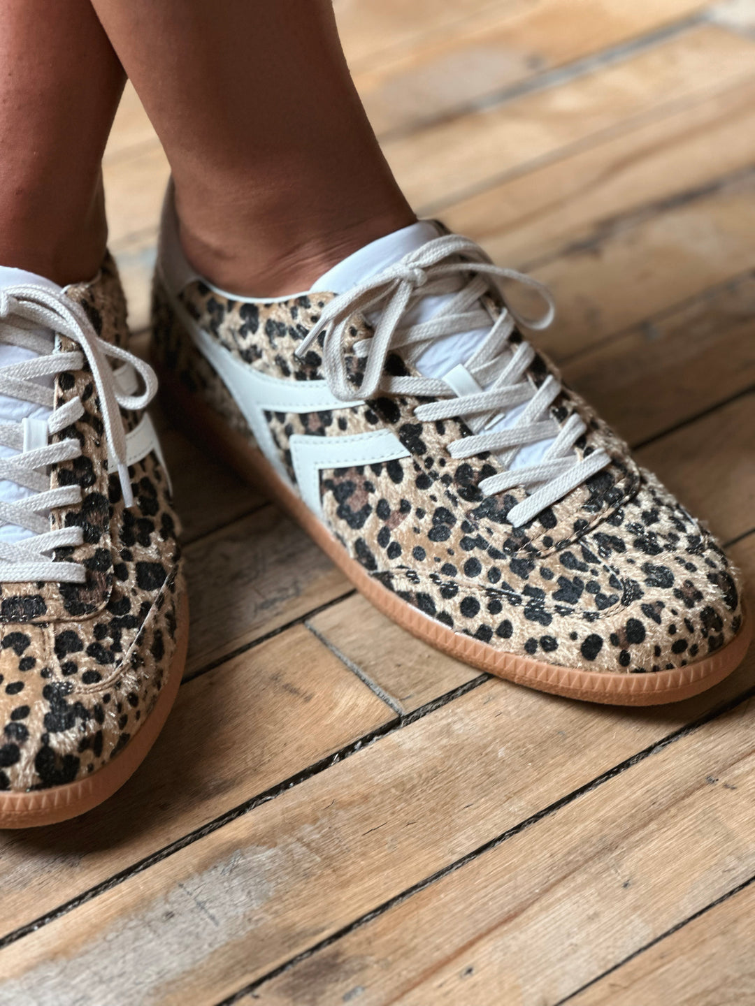 Leopard print sneakers with white laces on a wooden floor.