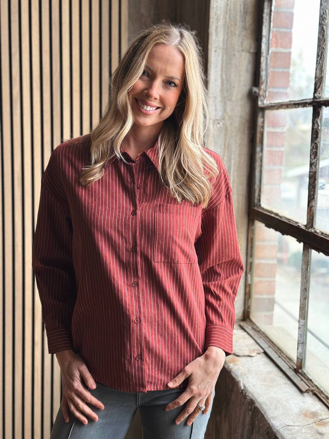 Woman wearing a red striped shirt standing by a window with a brick wall background