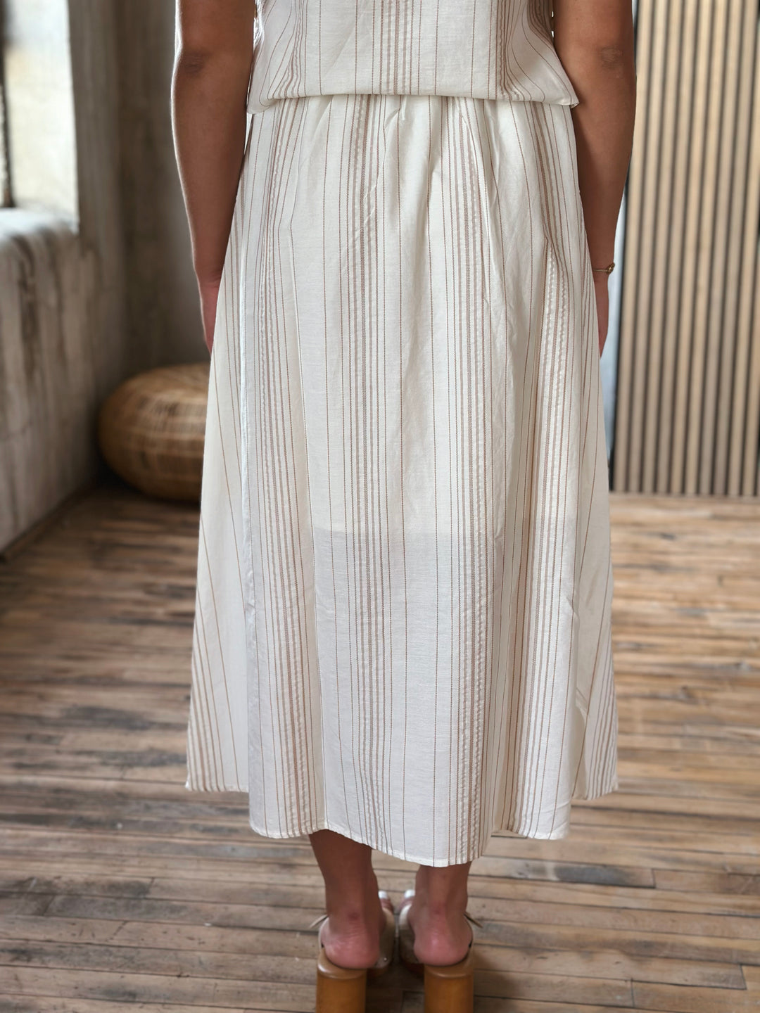 A person wearing a beige and white striped skirt standing on a wooden floor.