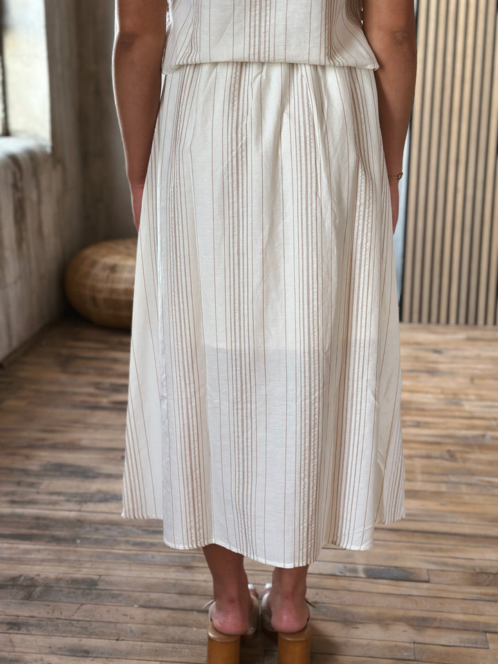 A person wearing a beige and white striped skirt standing on a wooden floor.