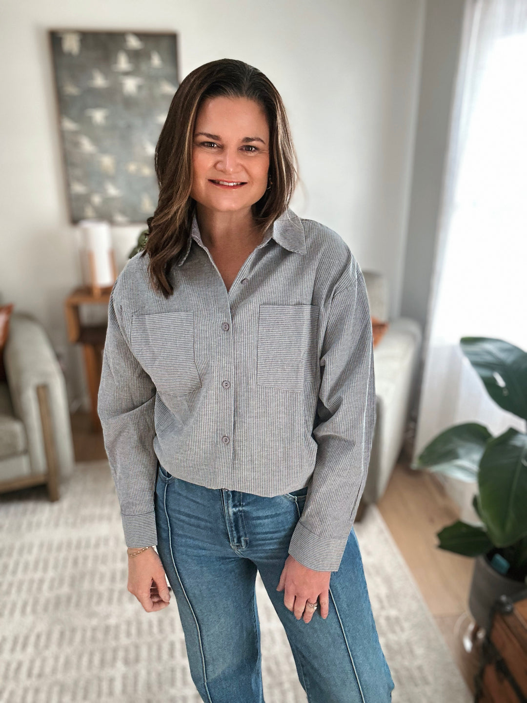 Woman wearing a gray striped shirt and blue jeans standing in a living room.