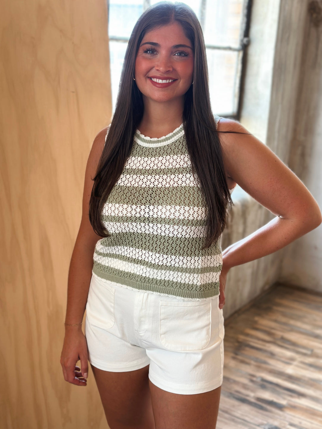 Woman wearing a green and white striped sleeveless top and white shorts indoors.