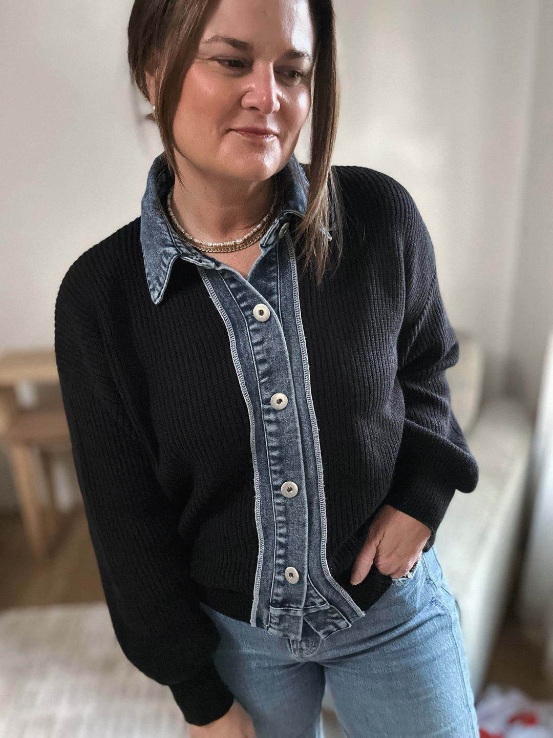 Woman wearing a black cardigan over a denim shirt with a blurred indoor background