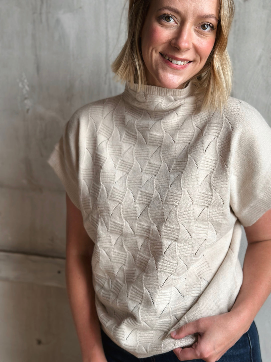 Woman wearing a beige knitted sleeveless sweater against a plain background