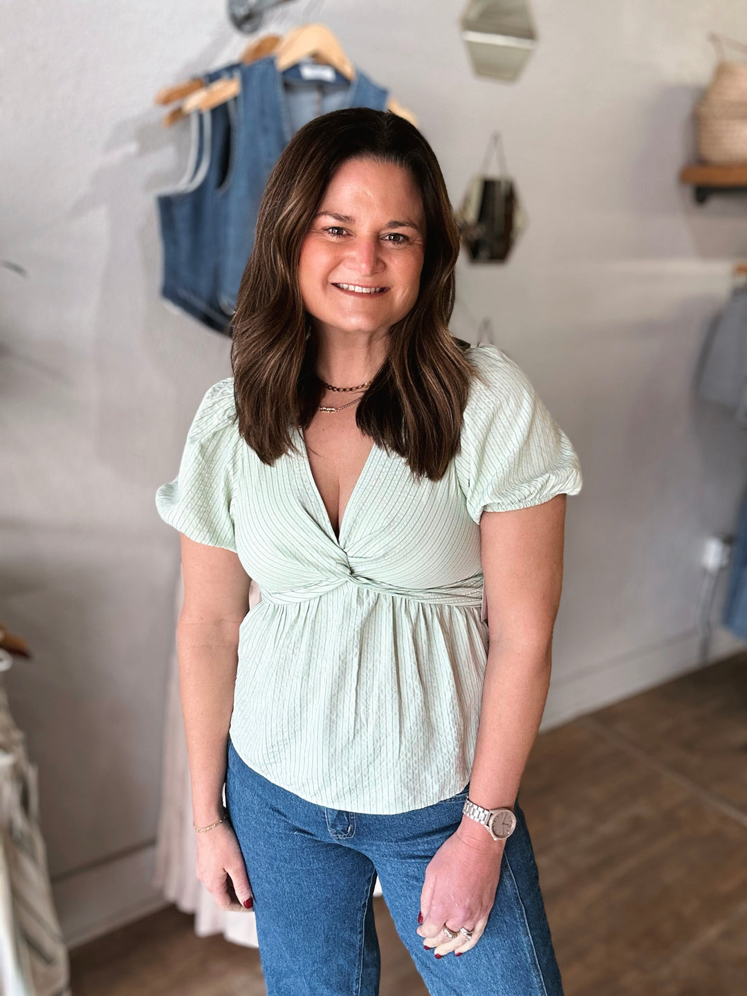 Woman wearing a light green top and blue jeans in a clothing store.