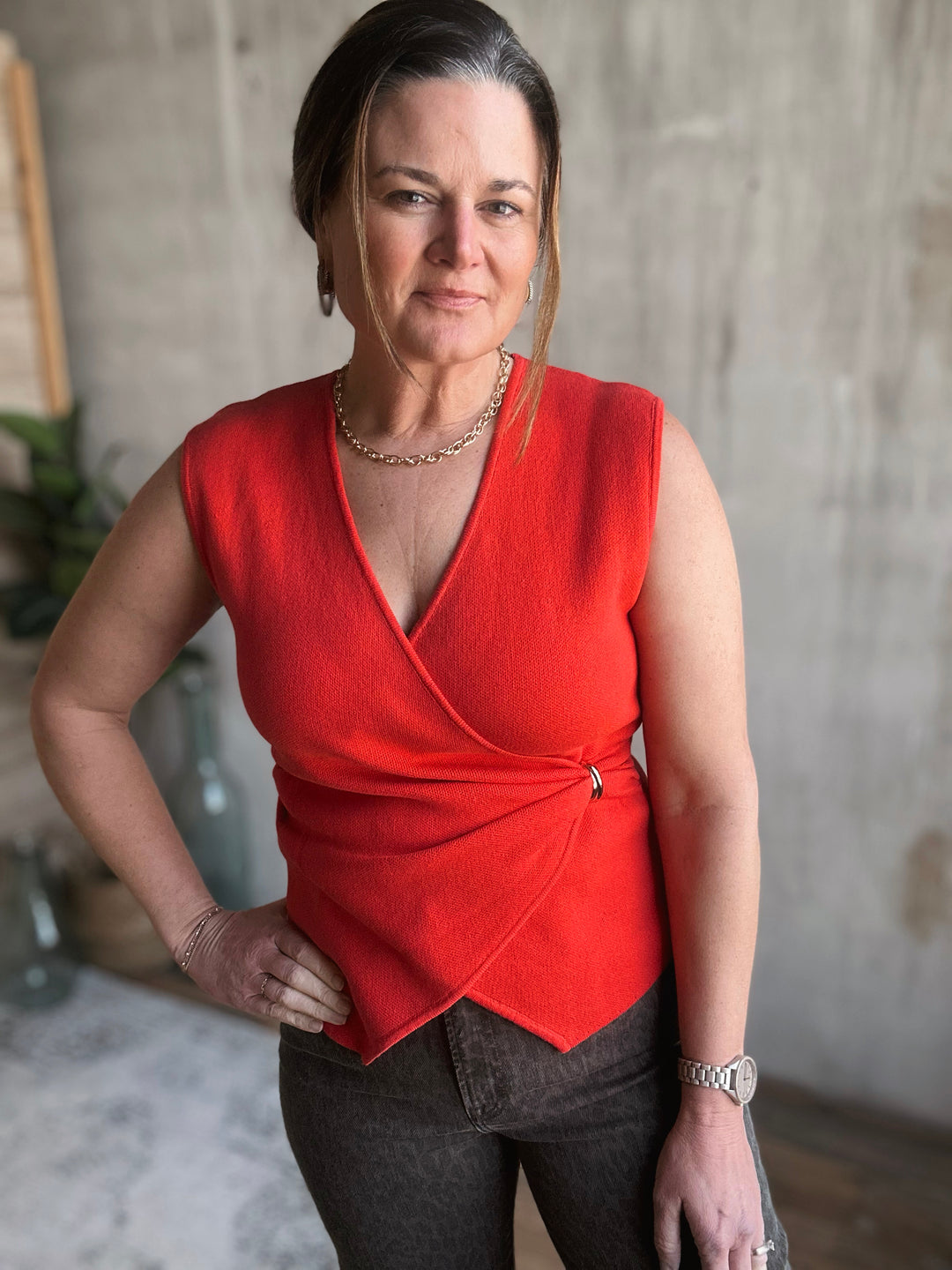 Woman wearing a red sleeveless top and dark pants indoors.