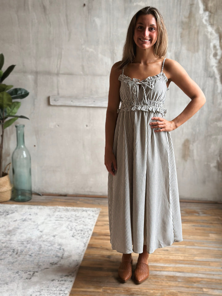 Woman wearing a white and gray striped dress standing in a room with a concrete wall and wooden floor.