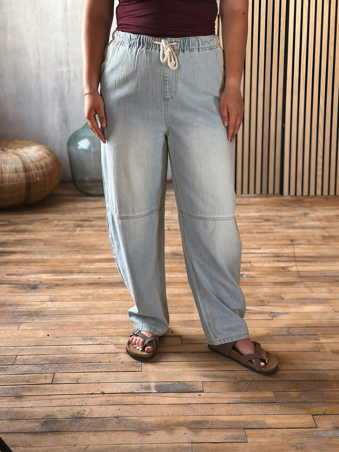 A person wearing light washed barrel jeans with a jaw string at the waist. 