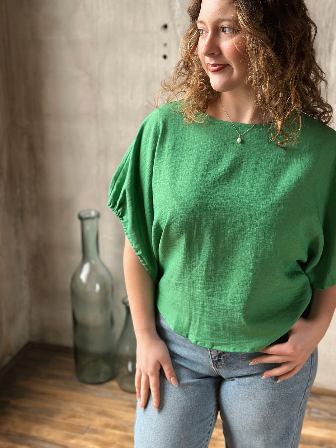 Woman wearing a green blouse standing in a room with a textured wall and a large bottle.