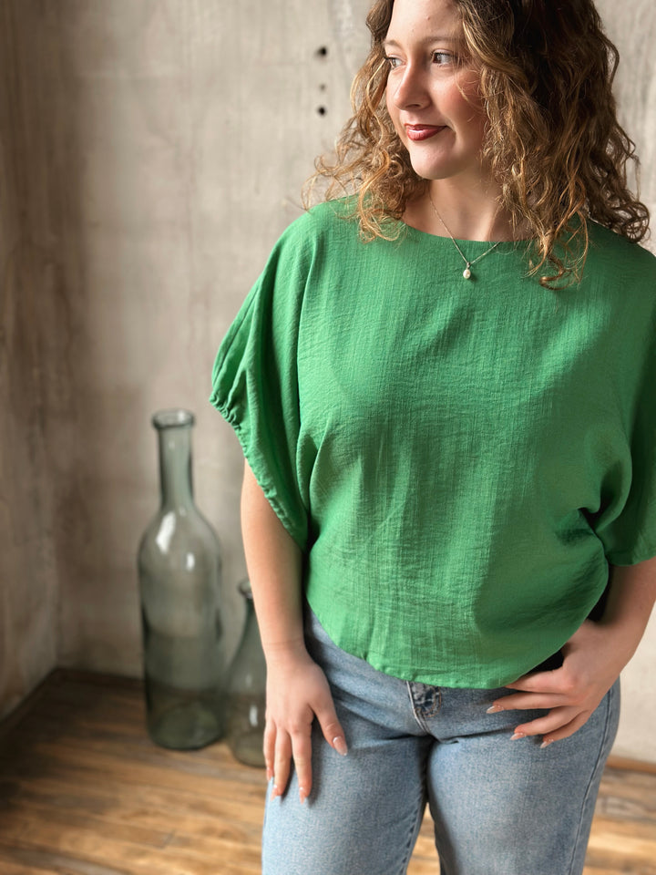 Woman wearing a green blouse standing in a room with a textured wall and a large bottle.