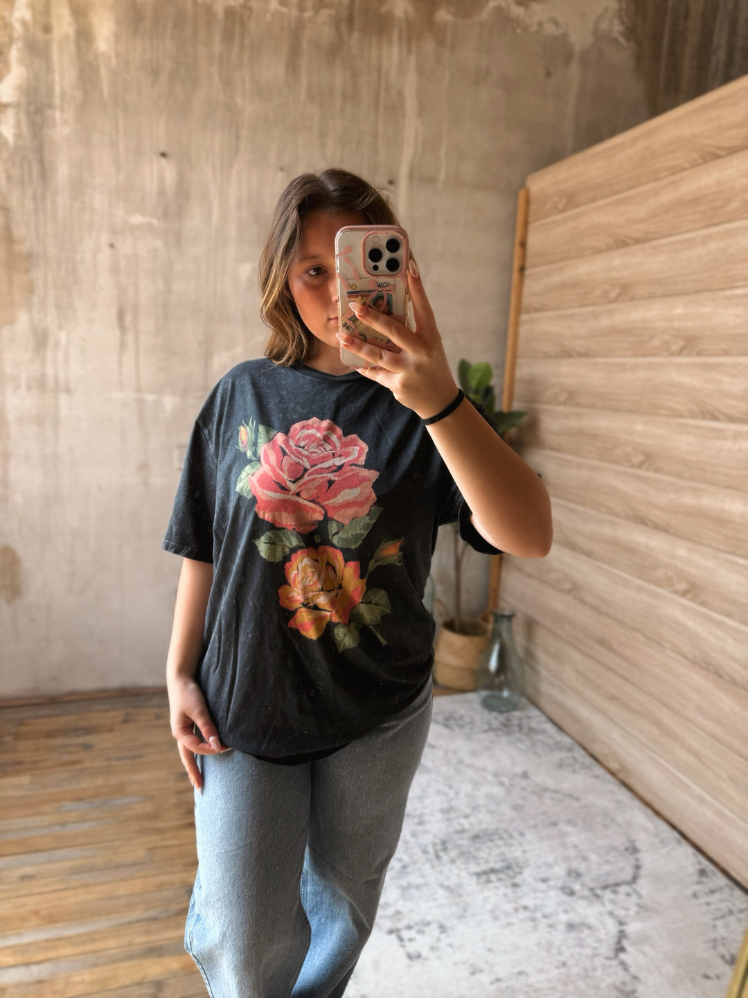 Person wearing a black t-shirt with floral designs in a room with wooden floor and wall.