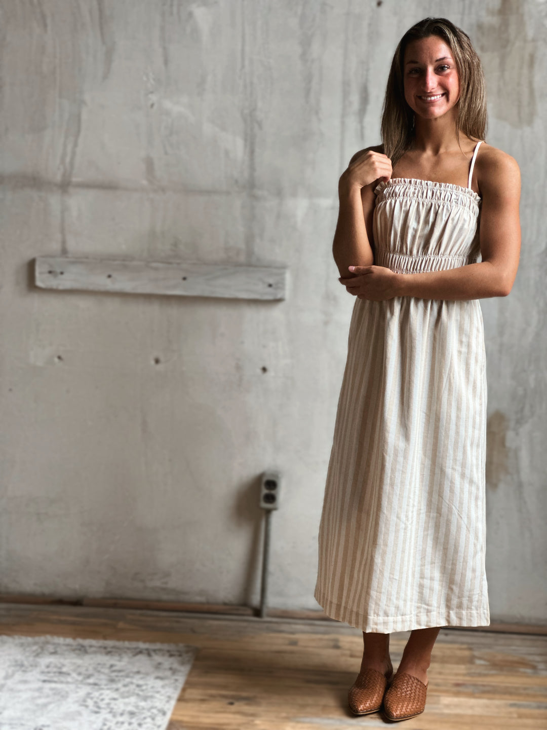 Woman wearing a white and cream striped dress standing in a room with concrete walls.