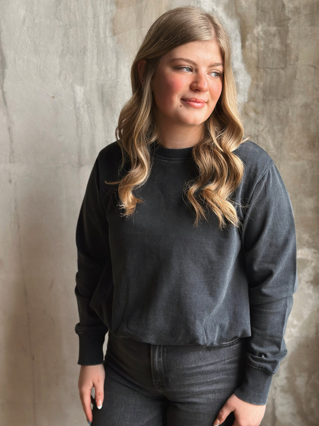 Woman wearing a black crew neck against a textured wall