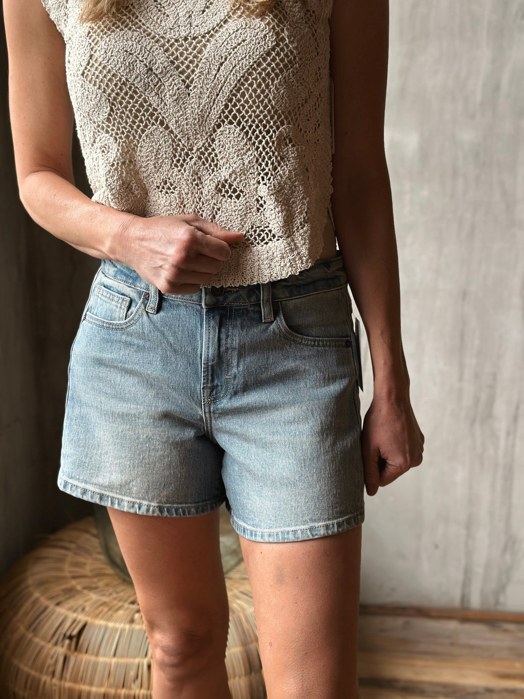 A person wearing a patterned top and light washed denim shorts against a neutral background.